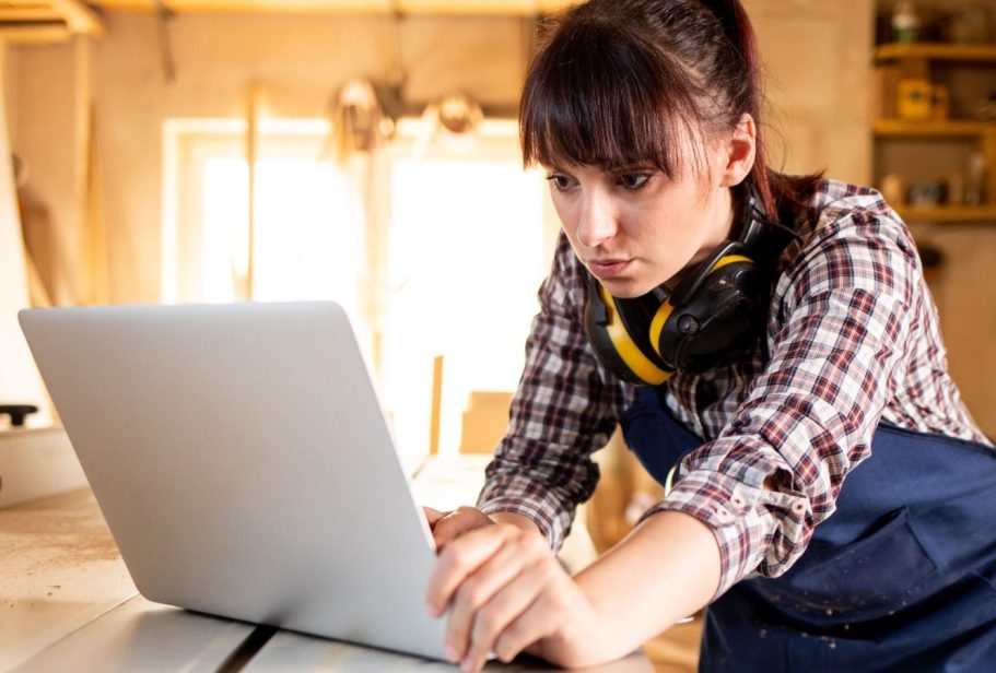 Junge Frau mit Kopfhörern arbeitet konzentriert am Laptop in einer Werkstatt.