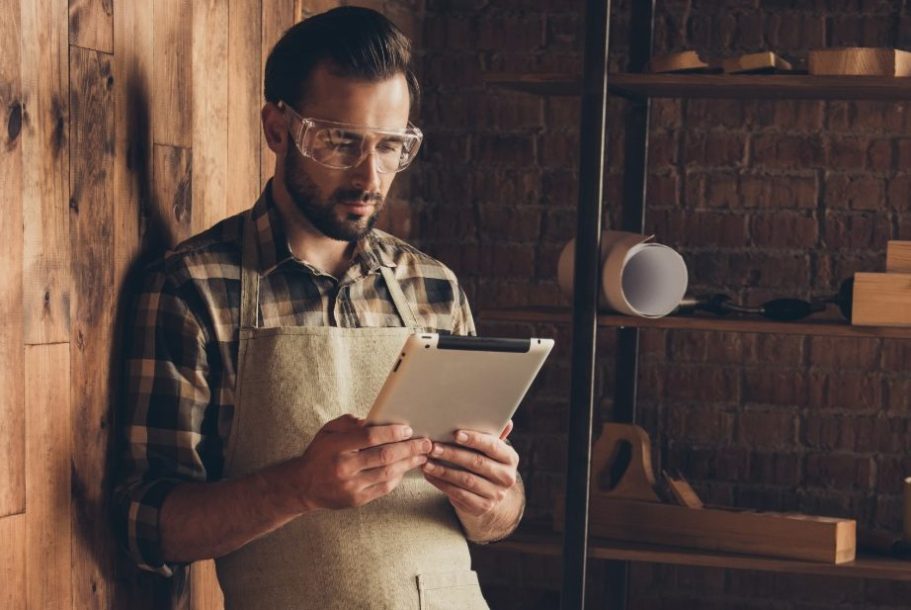 Mann in Arbeitskleidung steht an Wand und lernt mit seinem Tablet